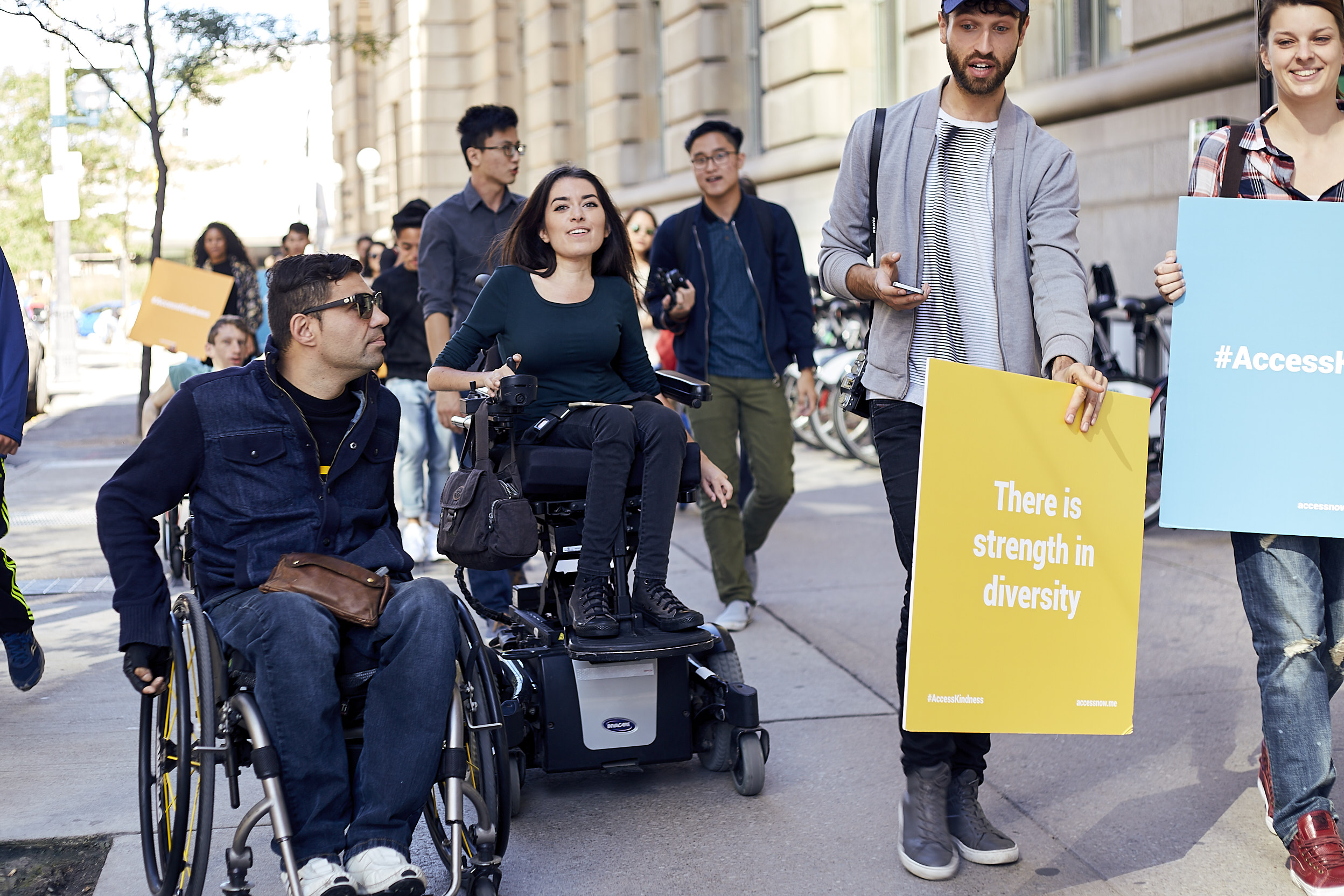 170909_ANIG_0129 a group of interabled people walk down a city sidewalk, some hold signs that say "you had me at accessible"